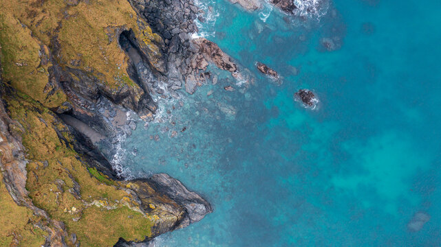Aerial view of rugged cliffs and turquoise sea at Hell's Mouth with rocky shoreline and grassy slopes Camborne, Cornwall, United Kingdom.