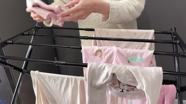 Women's hands collect and fold freshly washed children's clothes on a clothes dryer indoors.
