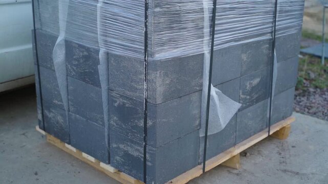 Stack of concrete blocks wrapped in plastic film on wooden pallet