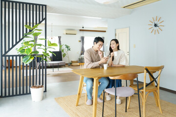 Fototapeta premium 自宅のテーブルでスマホを見ながら飲み物を飲む若い日本人パワーカップル