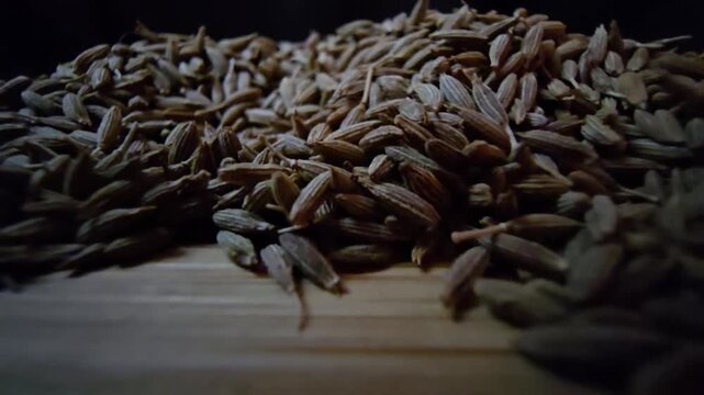 Macro close-up shot of dry cumin seeds scattered on a wooden surface, highlighting their texture and organic details.