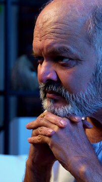 Senior Indian man deep thinking while sitting on sofa in bright airy modern home, thoughtful Asian elderly person with worried facial expression, old retired man lost in serious thoughts indoors