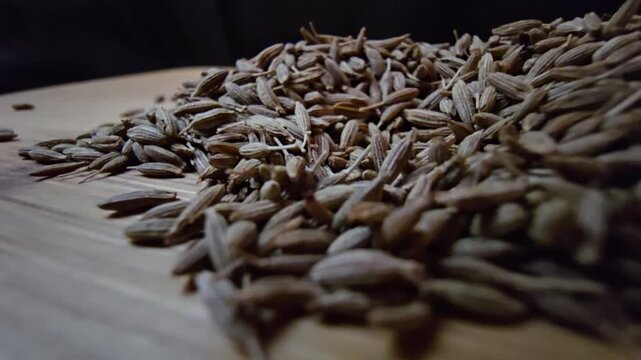 Macro close-up shot of dry cumin seeds scattered on a wooden surface, highlighting their texture and organic details.
