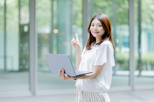 ノートパソコンを持ちながら指差しをする日本人女性