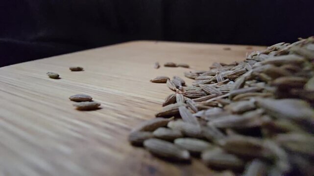 Macro close-up shot of dry cumin seeds scattered on a wooden surface, highlighting their texture and organic details.
