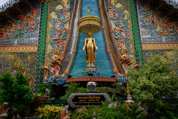 Fototapeta premium Stunning buddhist temple exterior with colorful mosaics and golden statue surrounded by lush greenery