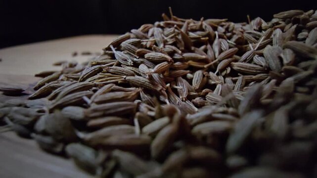 Macro close-up shot of dry cumin seeds scattered on a wooden surface, highlighting their texture and organic details.