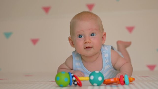 Three month old baby boy lying near rattle on soft mat. Slow motion.