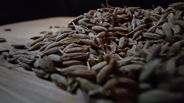 Close-up macro shot of organic raw cumin seeds scattered on a wooden surface, highlighting the textured details of the spice, perfect for culinary and healthy eating content.