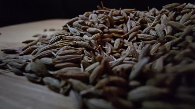 Macro close-up shot of dry cumin seeds scattered on a wooden surface, highlighting their texture and organic details.