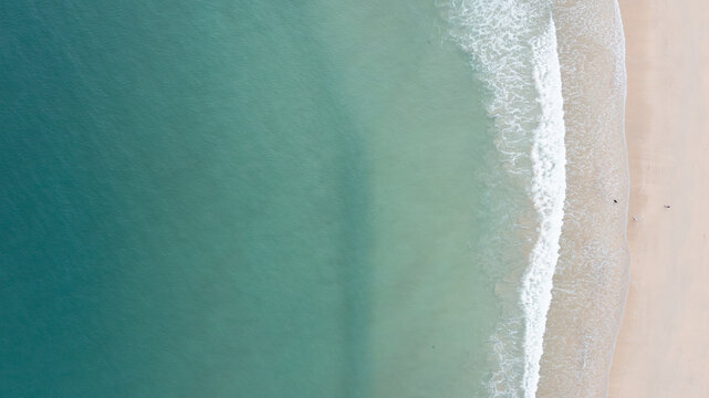 Aerial view of Harlyn Bay Beach featuring turquoise water and white waves crashing onto the sandy shore with tiny figures walking in Saint Merryn, Cornwall, United Kingdom.