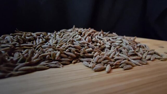 Macro close-up shot of dry cumin seeds scattered on a wooden surface, highlighting their texture and organic details.