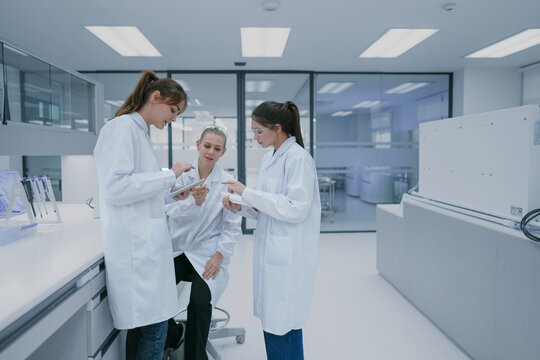 Clinical research associates (CRA) reviewing patient trial compliance data on mobile device. Medical team monitoring regulatory standards in hospital research center.