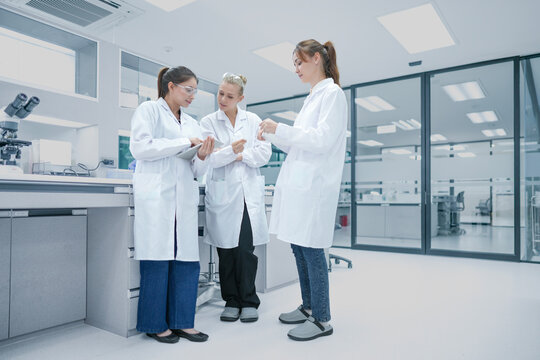 Clinical research associates (CRA) reviewing patient trial compliance data on mobile device. Medical team monitoring regulatory standards in hospital research center.