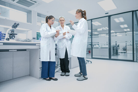 Clinical research associates (CRA) reviewing patient trial compliance data on mobile device. Medical team monitoring regulatory standards in hospital research center.