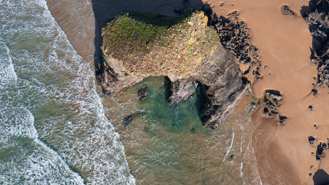Aerial view of the Bedruthan Steps rock formation on a sandy beach with waves crashing against the shore in Padstow, Cornwall, United Kingdom.