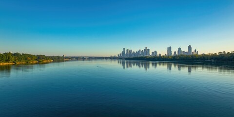 Fototapeta premium City skyline reflected in calm river water under blue sky