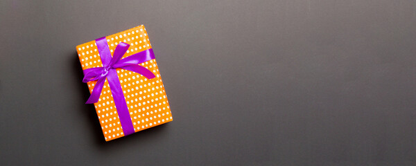 Obraz premium wrapped Christmas or other holiday handmade present in paper with purple ribbon on black background. Present box, decoration of gift on colored table, top view with copy space