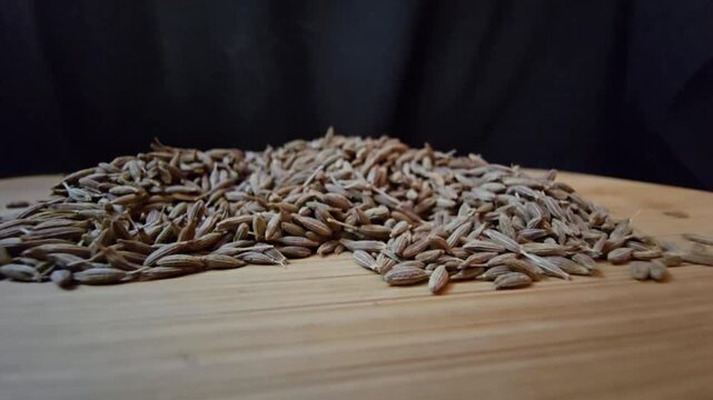 Close-up macro shot of organic raw cumin seeds scattered on a wooden surface, highlighting the textured details of the spice, perfect for culinary and healthy eating content.