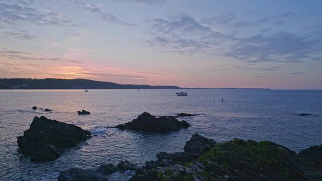 Fishing boat  head out to sea from the harbor area near the rugged coastline in the early morning light at dawn over the water in Looe Cornwall, United Kingdom