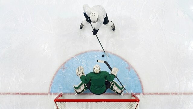 Ice hockey player attacking goal against goalkeeper from overhead view. Concept of professional hockey competition, goal scoring and tactical sports performance.