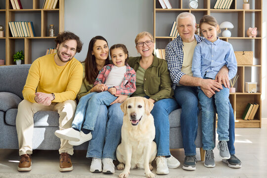 Family grandparents parents children dog together at home. Three generations sitting with labrador, smiling at camera in living room portrait. Clear concept family love across generations.