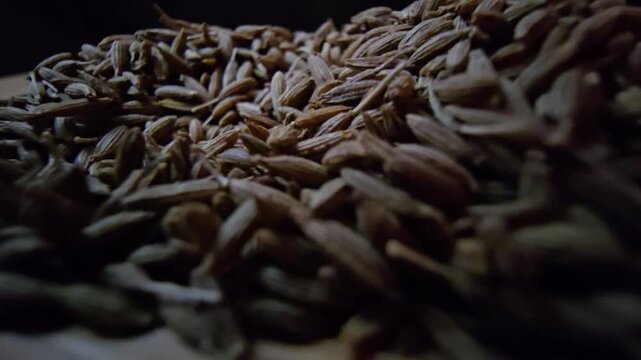 Close-up macro shot of organic raw cumin seeds scattered on a wooden surface, highlighting the textured details of the spice, perfect for culinary and healthy eating content.
