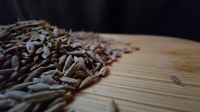 Close-up macro shot of organic raw cumin seeds scattered on a wooden surface, highlighting the textured details of the spice, perfect for culinary and healthy eating content.