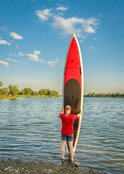 male paddler with his long stand up paddleboard on a lake shore