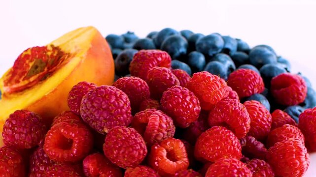 Fresh raspberries blueberries and a slice of cantaloupe on a white background