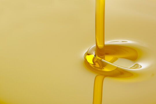 Close-up of golden vegetable oil pouring and creating ripples with oil stream liquid motion food preparation cooking oil kitchen ingredient close-up culinary

