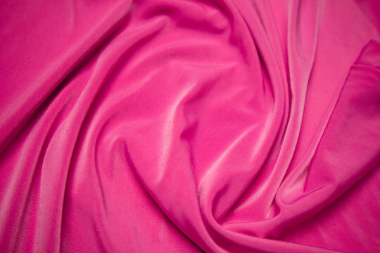 Full frame flat lay view of vibrant pink fabric featuring elegant flowing drapery with curved organic folds and soft wave textures