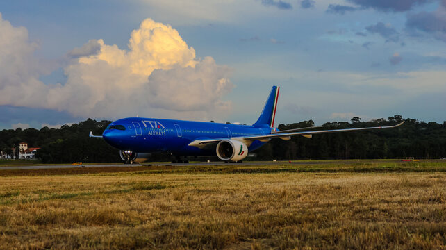 Jato comercial da ITA Airways em deslocamento no Aeroporto de Guarulhos, com pintura azul, pista e nuvens ao fundo, em Guarulhos, SP, 10 de maio de 2026.