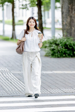 コーヒーを片手にオフィス街を歩く日本人女性