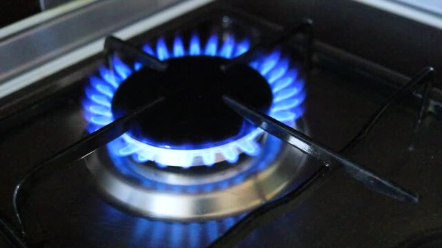 Blue gas flame burning on household kitchen stove in dark interior, close up view of natural gas consumption, domestic energy use, rising gas prices, utility bills, energy crisis, inflation, household