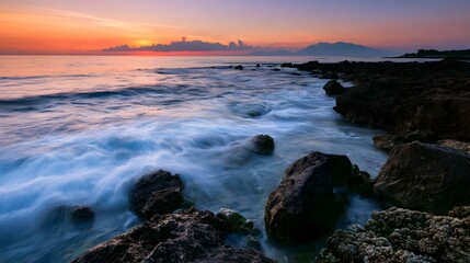 Fototapeta premium A calm rocky coastline features a distant horizon with foamy coral reefs under vibrant sunset hues