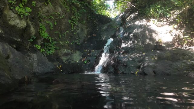 The top small pool in Gembleng Waterfall in Sideman, Bali. A slow motion dolly towards the cascade of water, a small frog sits at the side. Sunshine and reflections. 
