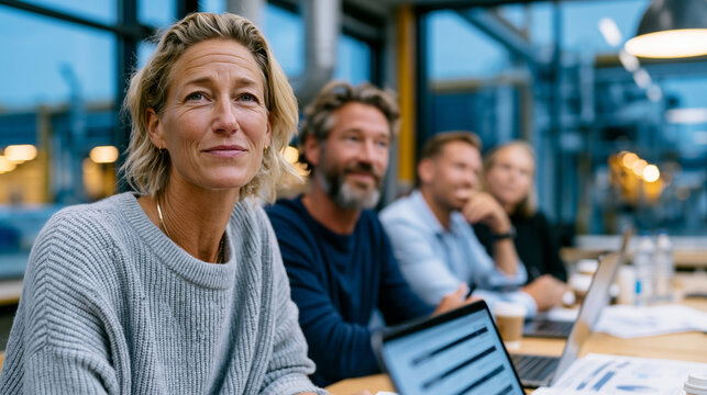 A realistic post-pilot project debrief in an industrial company canteen after hours, four professionals in business casual sitting on one side of a long canteen table with laptops