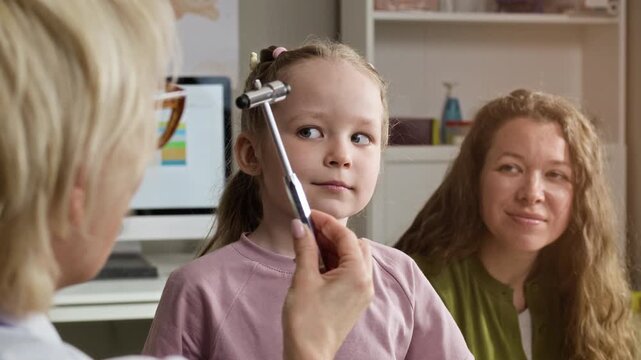 Medium closeup of Caucasian female pediatrician testing eye coordination of Caucasian female child using reflex hammer during medical checkup. Ideal for pediatric healthcare marketing