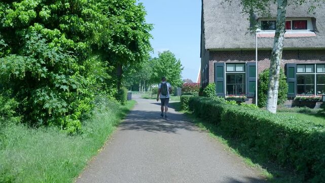 Man with backpack walking along a country road in a dutch village
