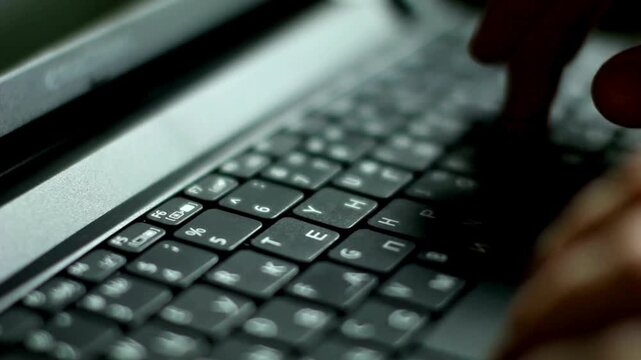 Close-up laptop keyboard, hand on computer keys, typing on black keyboard with white text