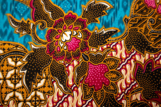 Close-up macro flat lay view of traditional Indonesian batik fabric with detailed floral ornaments and parang motif on blue background