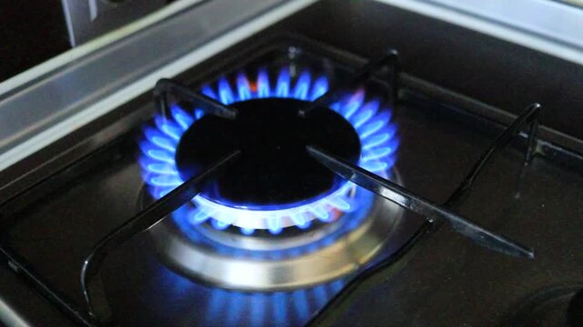 Gas burner igniting on kitchen stove in dark interior, close up of blue natural gas flame appearing on household cooker, domestic energy use, cooking appliance, gas consumption, utility bills, rising