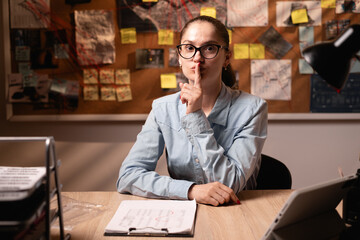 Obraz premium Female detective showing shhh sign shush working overwork in her dark office