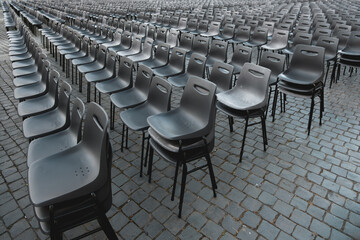 Fototapeta premium Rows of empty gray plastic chairs arranged outdoors on cobblestone pavement, ideal for event seating, ceremony setup, or conference preparation