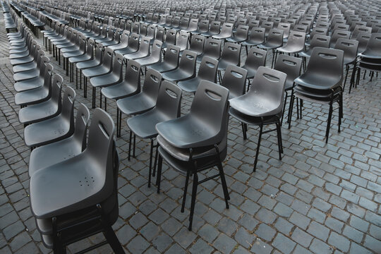 Rows of empty gray plastic chairs arranged outdoors on cobblestone pavement, ideal for event seating, ceremony setup, or conference preparation
