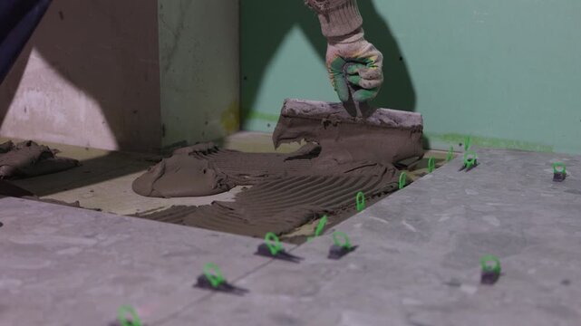 Applying tile adhesive with notched trowel during floor tile installation