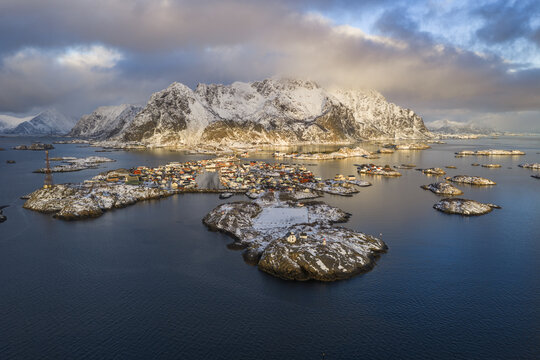 Aerial view of the Henningsvaer village and football pitch on rocky islands with snow-covered mountains in Norway.