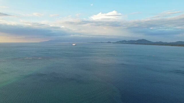Aerial drone footage of Lembar beautiful bay, in Lombok island, Indonesia, with the coast leading to Mataram city, some coral reef, a ferry boat, at sunset with clouds