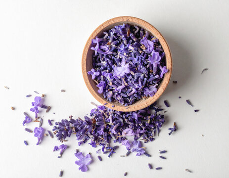 A wooden bowl filled with dried lavender flowers, spilling onto a white surface around its base.